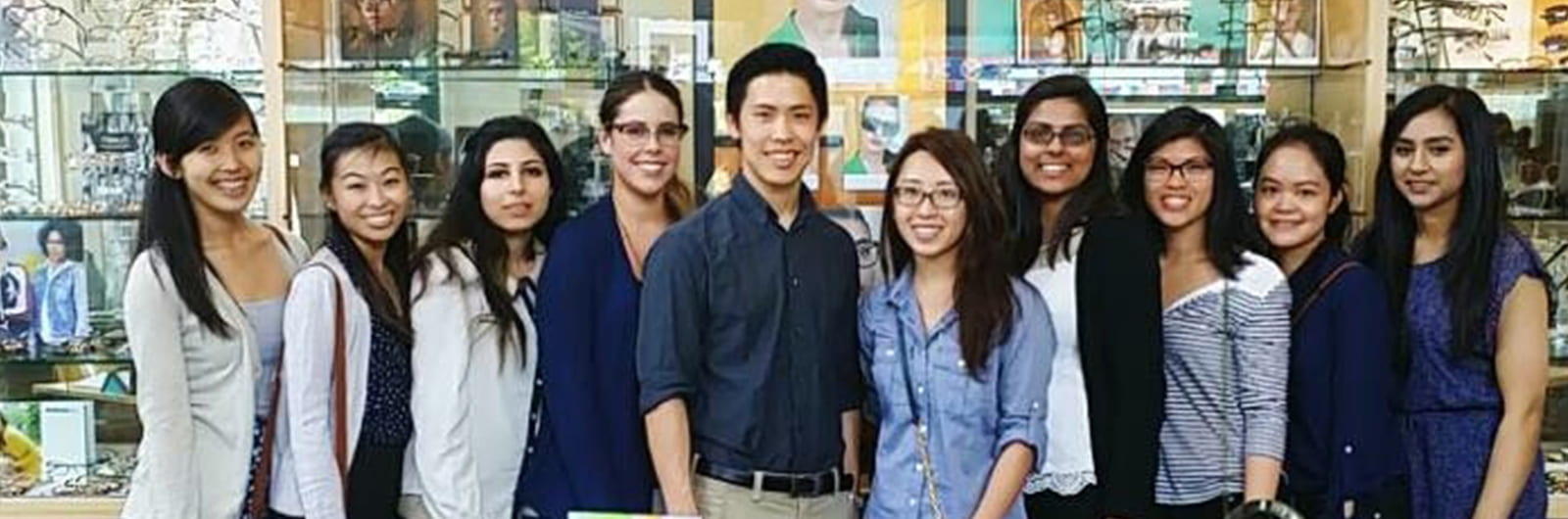 A photo of ten students in front of glass shelves full of eyeglasses.
