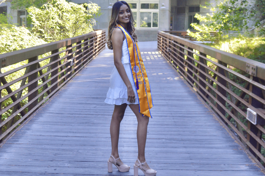 Photo of Sneha standing on a bridge of the UC Santa Cruz campus, wearing her graduation stole.